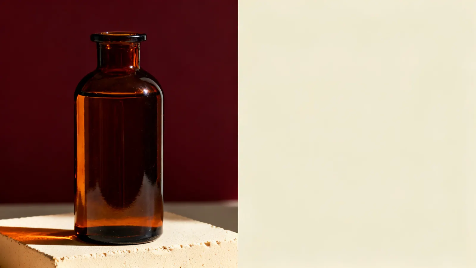 Natureza-morta em luz lateral dura: um frasco alto de vidro transparente, sobre fundo vinho e creme