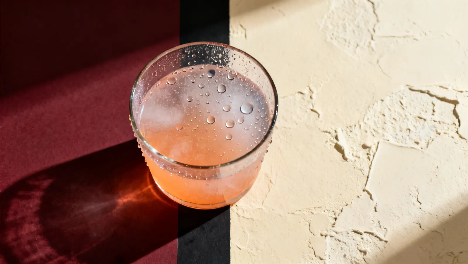 Natureza-morta em luz lateral dura: condensacao fria em gotas sobre vidro e gotas de agua suspensas, sobre fundo vinho e creme