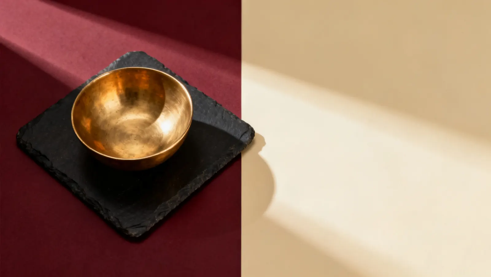 Natureza-morta em luz lateral dura: uma tigela lisa de latao, sobre fundo vinho e creme