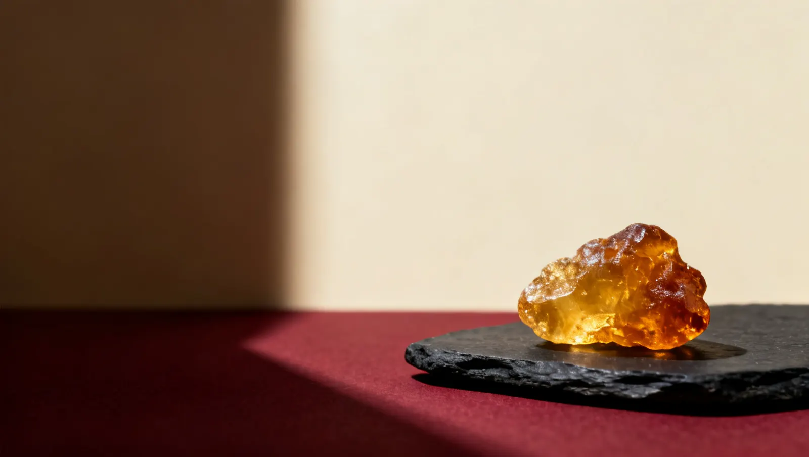 Natureza-morta em luz lateral dura: um bloco de resina de ambar dourado, sobre fundo vinho e creme