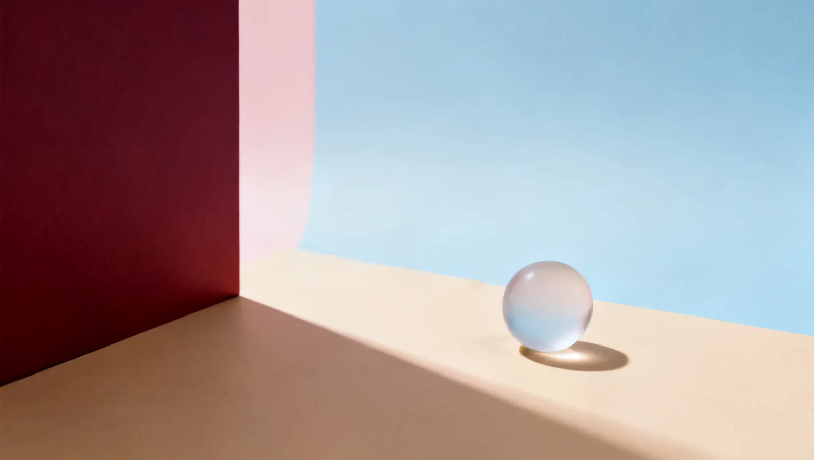 Natureza-morta em luz lateral dura: uma esfera pequena de vidro fosco, sobre fundo vinho e creme