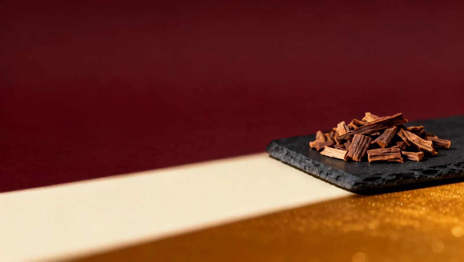 Natureza-morta em luz lateral dura: lascas de madeira de oud, sobre fundo vinho e creme